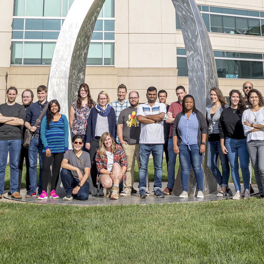 Group photo of postdoctoral researchers standing near double helix statue on the Stowers Institute campus.